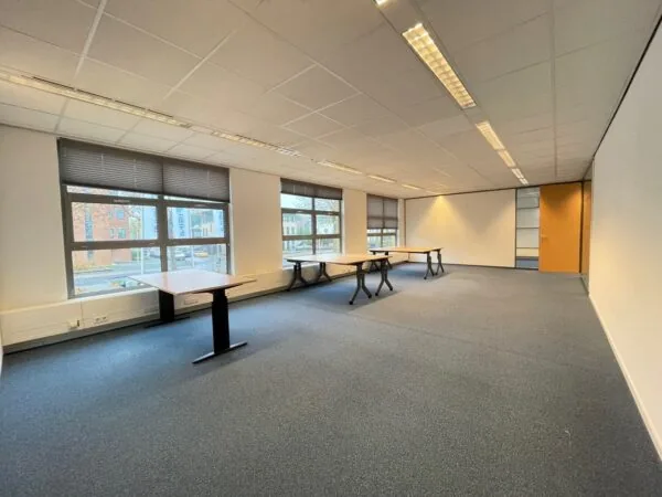 Licht kantoorruimte aan de Rivium 3e Straat met grote ramen, systeemplafond en enkele bureaus.